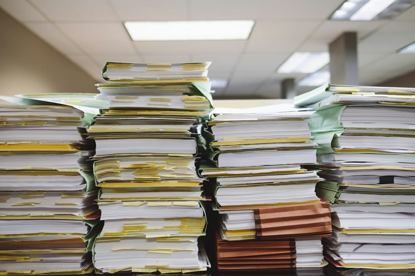Overstuffed paper case files stacked high on a desk in a fluorescent-lit office.